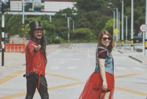 Dos personas con vestuario urbano y colorido caminan en la calle de alguna ciudad.