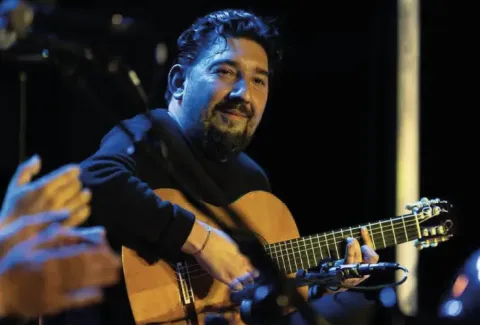 Hombre tocando la guitarra frente a un micrófono y un micrófono