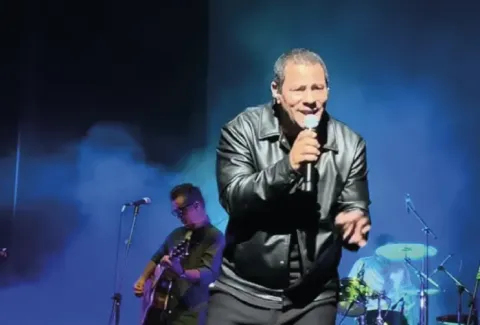Hombre con chaqueta de cuero cantando frente a un micrófono.