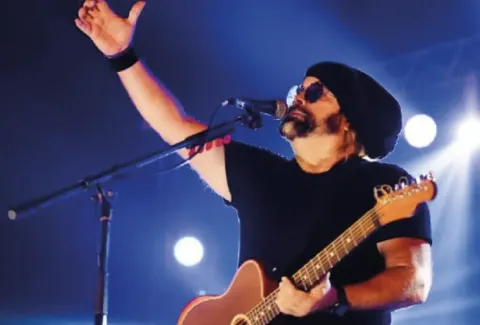 Hombre con una guitarra y un sombrero en un escenario