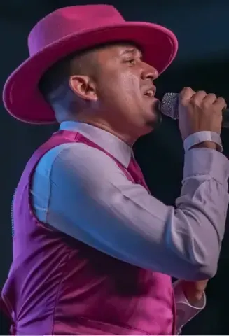 Hombre con sombrero y chaleco fucsia cantando en micrófono en el Teatro Colsubsidio.