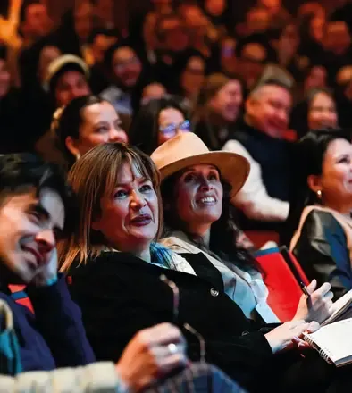 Audiencia diversa en un evento de Teatro Colsubsidio, sonriendo y atenta, algunos tomando notas.