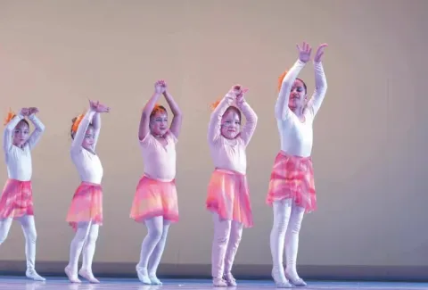 Cinco niñas bailando, con brazos alzados y vestidas de blanco y rosa, en una presentación de danza en Teatro Colsubsidio.