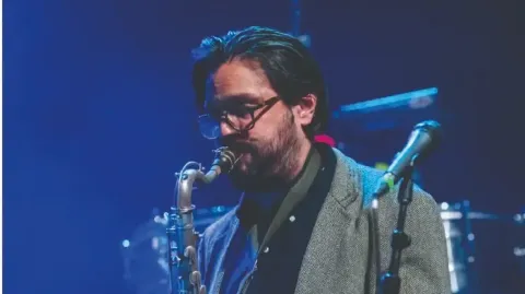Músico con saxofón en el Teatro Colsubsidio interpreta bajo luces azules.