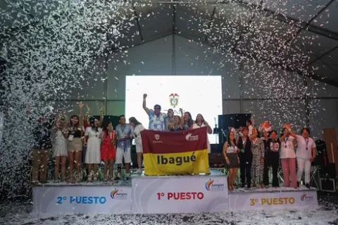 Personas felices celebran en podio de premiación del Teatro Colsubsidio. Muestran bandera de Ibagué.