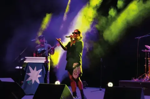 Concierto en vivo: cantante con micrófono y gafas de sol en el Teatro Colsubsidio.