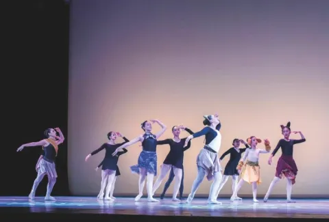 bailarines en el escenario, algunos con orejas de animales, realizan una coreografía.