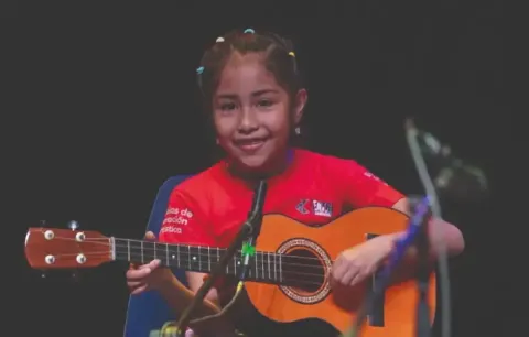 Niña en el Teatro Colsubsidio toca guitarra acústica en escena.