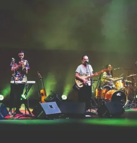 Tres músicos en el Teatro Colsubsidio interpretan trompeta, guitarra y batería.