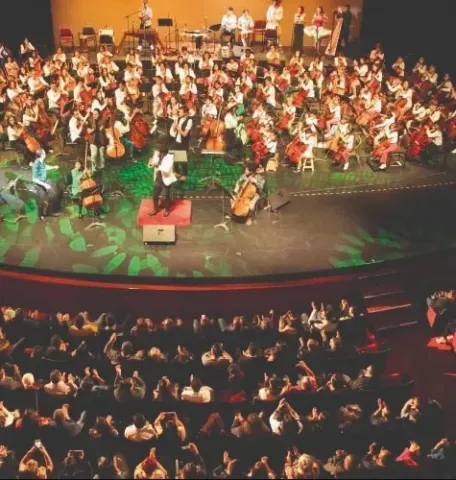 Gran orquesta en el Teatro Colsubsidio dirigida por un director, con cuerdas y percusión.