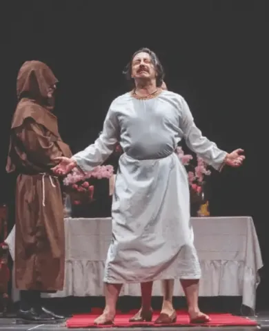 Actores en el Teatro Colsubsidio con vestuarios religiosos y mesa con flores.