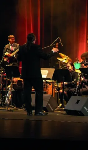 Director musical de espaldas dirige banda en escenario.