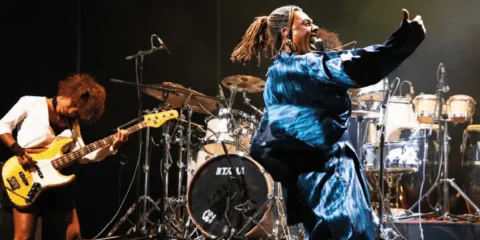 Concierto en el Teatro Colsubsidio con bajista, cantante en traje azul brillante y percusión.