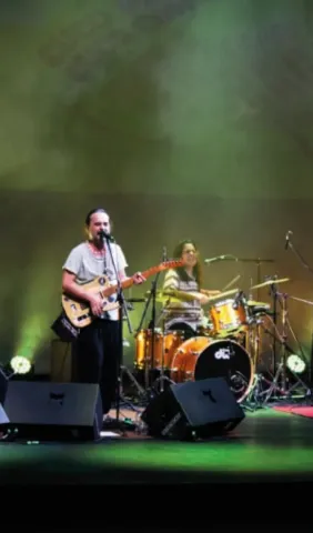 Músicos tocando en vivo: guitarrista cantando y baterista en escenario.