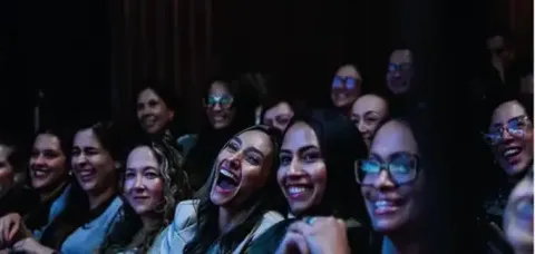 Mujeres riendo y sonriendo animadamente, con una mujer en primer plano riendo a carcajadas en el Teatro Colsubsidio.