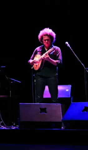  Músico con cabello rizado rojo tocando instrumento de cuerda en escenario.