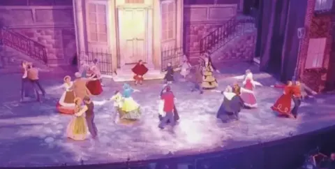 Bailarines en el Teatro Colsubsidio con vestuarios coloridos en escenario urbano.