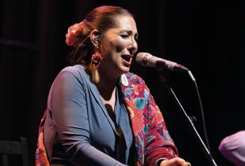 Mujer cantando frente a un micrófono mientras está sentada en una silla.