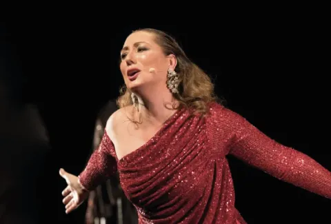 Mujer con un vestido rojo cantando en el escenario con un micrófono.