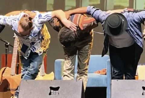 Varias personas están de pie en el escenario con las manos en las caderas.