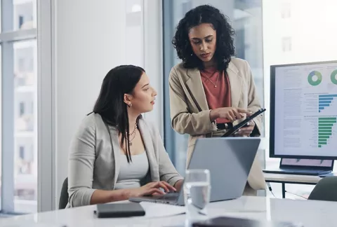 Dos mujeres profesionales revisan datos y gráficos en una tablet y computador durante un curso de pensamiento estratégico.