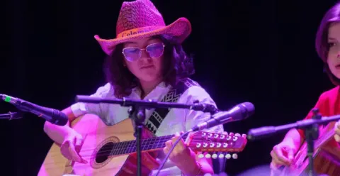 Joven con sombrero tipleño tocando un tiple durante un concierto de música colombiana.