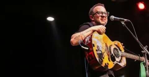 César López tocando su guitarra intervenida en un escenario iluminado.
