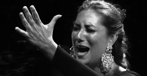 Cantaora con expresión apasionada, mano levantada y grandes pendientes, en blanco y negro.