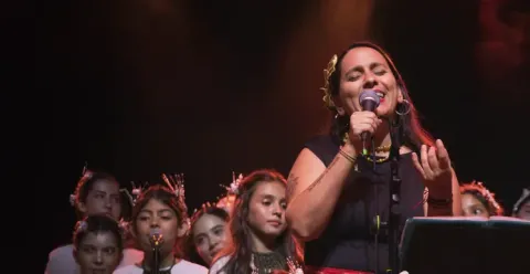 Marta Gómez cantando de cerca con micrófono frente al coro infantil Cantoalegre.