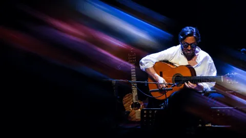 Al Di Meola sonriendo mientras toca la guitarra acústica durante su presentación.