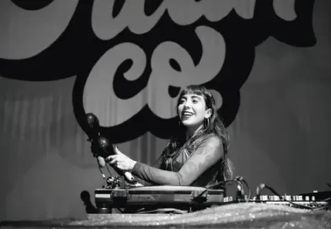 Mujer sonriente tocando las maracas frente a un tornaequipo en el escenario.