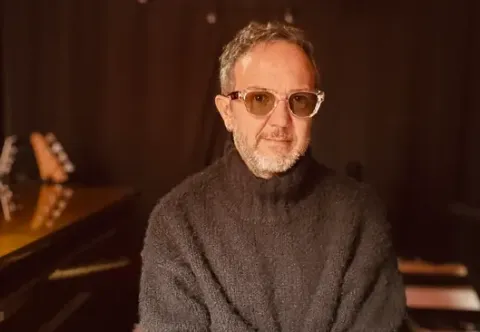 Retrato del músico César López con gafas y saco negro en su estudio.
