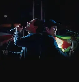 Integrantes del dúo Buena Fe cantando y tocando la guitarra de espaldas en el escenario.