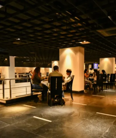 Personas compartiendo en mesas en un salón de restaurante iluminado con cielo raso reticulado.