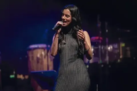 Mujer cantando apasionadamente frente a un micrófono durante una presentación de jazz.