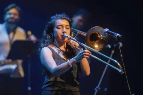 Mujer interpretando concentrada un solo de trombón en el escenario.