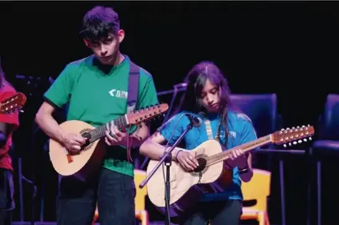 Dos jóvenes tocando bandola y tiple concentrados en una presentación musical.