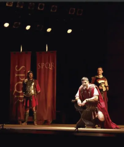 Actores caracterizados como romanos en el escenario junto a estandartes con las siglas SPQR.