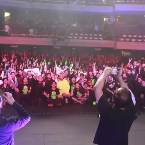 Fotógrafo capturando una foto grupal de una banda con el público de fondo en el teatro.
