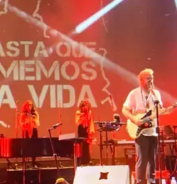 César López tocando la guitarra en vivo junto a sus coristas en el escenario.