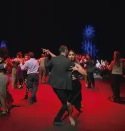Pareja bailando tango en primer plano en una pista rodeada de bailarines.