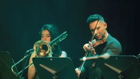 Violinista y trombonista interpretando sus instrumentos en vivo sobre el escenario.