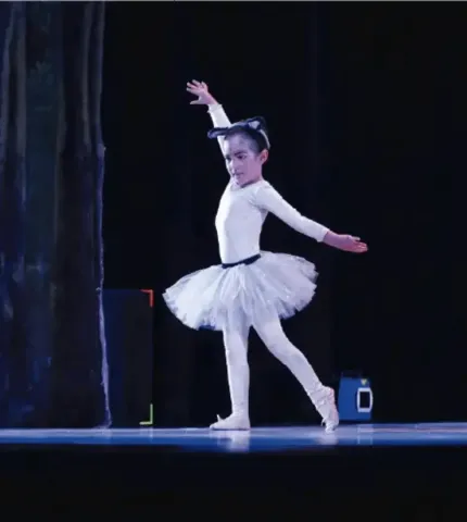 Niña bailarina realizando una postura de ballet clásico sobre el escenario.