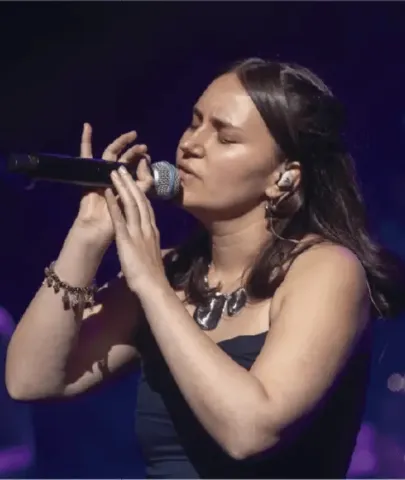Cantante interpretando un tema con micrófono e in-ears bajo la iluminación del escenario.