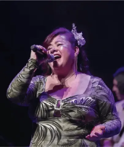 Cantante con vestido estampado interpretando apasionadamente una canción en vivo.