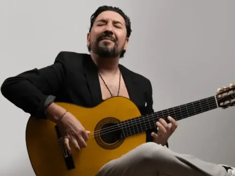 Guitarrista con traje oscuro interpretando una guitarra acústica con expresividad.