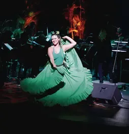 Bailarina con vestido verde ondeando su falda larga en una presentación de danza sobre el escenario.