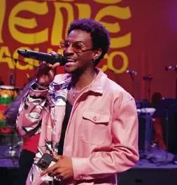 Cantante con chaqueta rosada e gafas interpretando una canción con micrófono en vivo.