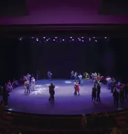 Vista general del escenario de un teatro con varias parejas bailando milonga.