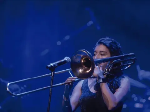 Mujer interpretando concentrada un solo de trombón en el escenario.